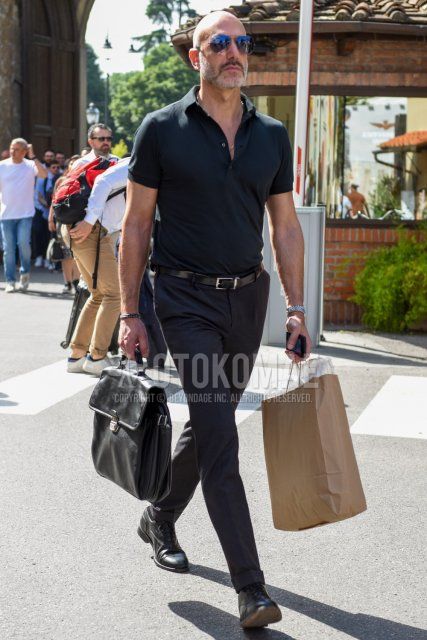 Men's spring/summer outfit with teardrop solid silver sunglasses, solid black polo shirt, solid black leather belt, dark gray solid slacks, black plain toe leather shoes, and solid black briefcase/handbag.