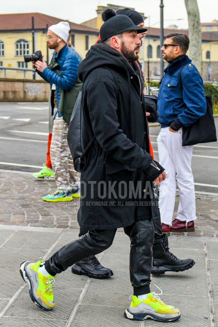 Winter men's coordinate and outfit with plain black cap, plain black hooded coat, plain black bottoms, plain black jogger pants/ribbed pants, plain white socks, Balenciaga Triple S yellow low-cut sneakers, and plain black backpack.