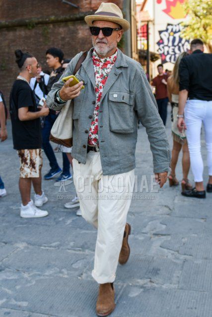 Men's spring/fall outfit with solid beige hat, solid black sunglasses, solid gray safari jacket, white top/inner shirt, solid black tape belt, solid white chinos, suede beige side gore boots, solid beige tote bag.