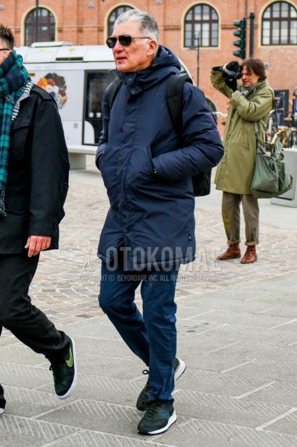 Winter men's coordinate and outfit with solid color sunglasses, solid color navy down jacket, solid color blue cotton pants, and green low-cut New Balance sneakers.