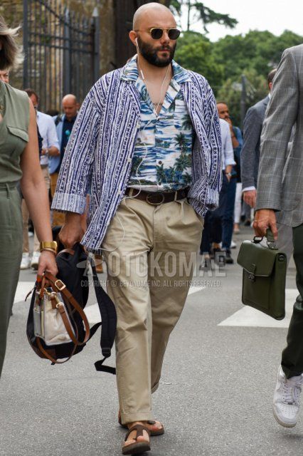 Men's spring/summer coordinate and outfit with gold/black solid sunglasses, blue/white outer tailored jacket, open collar multi-colored graphic shirt, brown solid leather belt, beige solid chinos and brown leather sandals.