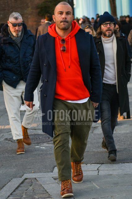 Men's fall/winter outfit with plain navy chester coat, plain red hoodie, plain olive green chinos, plain olive green ankle pants, and brown work boots.