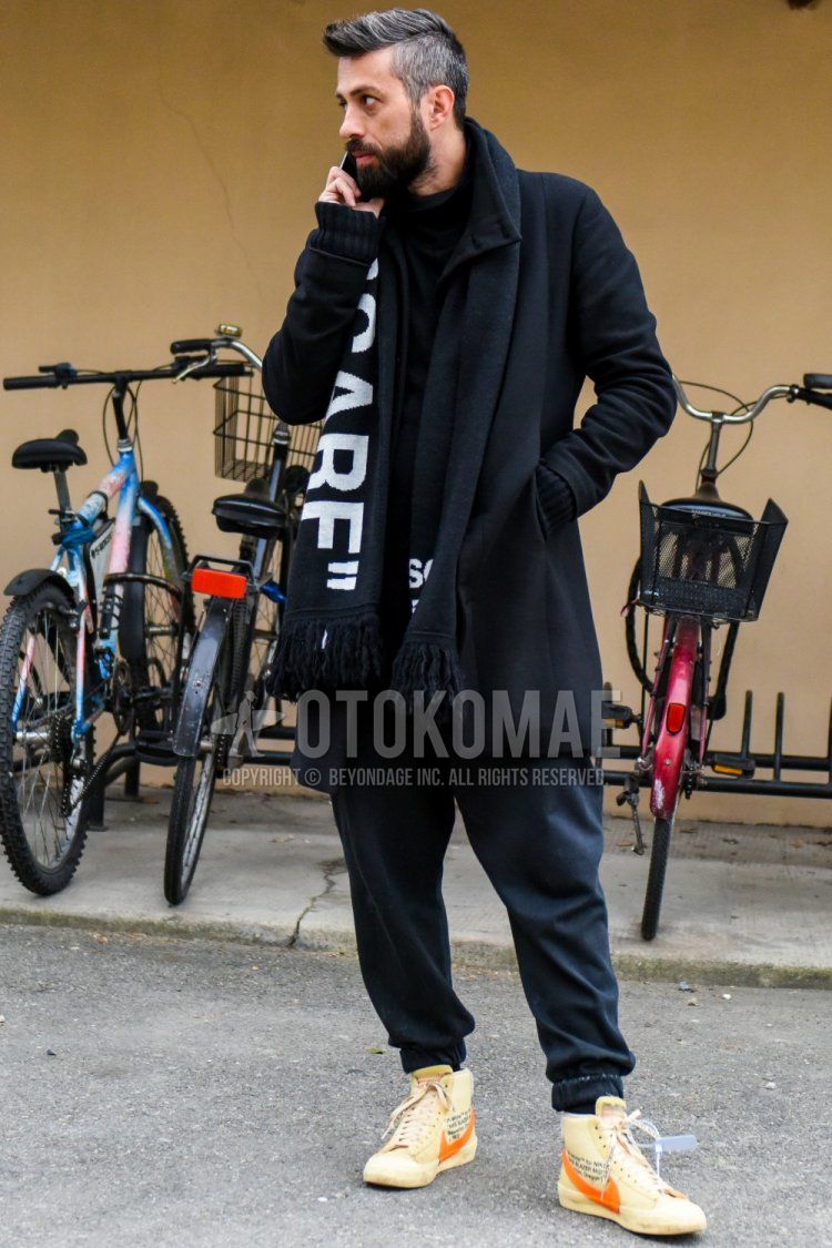 Winter men's coordinate and outfit with black graphic scarf/stall, solid black outerwear, solid black sweater, solid black sweatpants, and Nike orange high-cut sneakers.