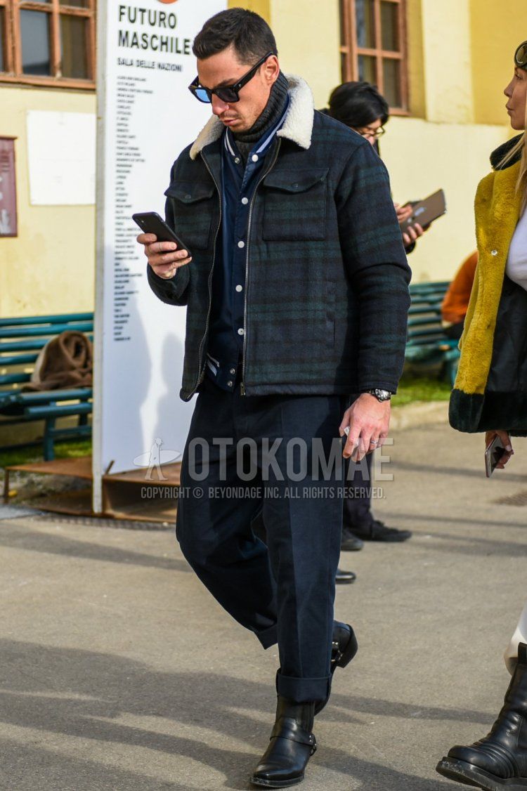 黒べっ甲のサングラス、オリーブグリーン・ネイビーチェックのトラッカージャケット、ネイビー無地のスタジャン、ネイビー無地のコットンパンツ、黒のブーツを合わせた秋冬のメンズコーデ・着こなし。