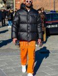 Winter men's coordinate and outfit with orange one-pointed knit cap, plain white sunglasses, plain black down jacket, orange graphic sweatpants, and white low-cut sneakers.