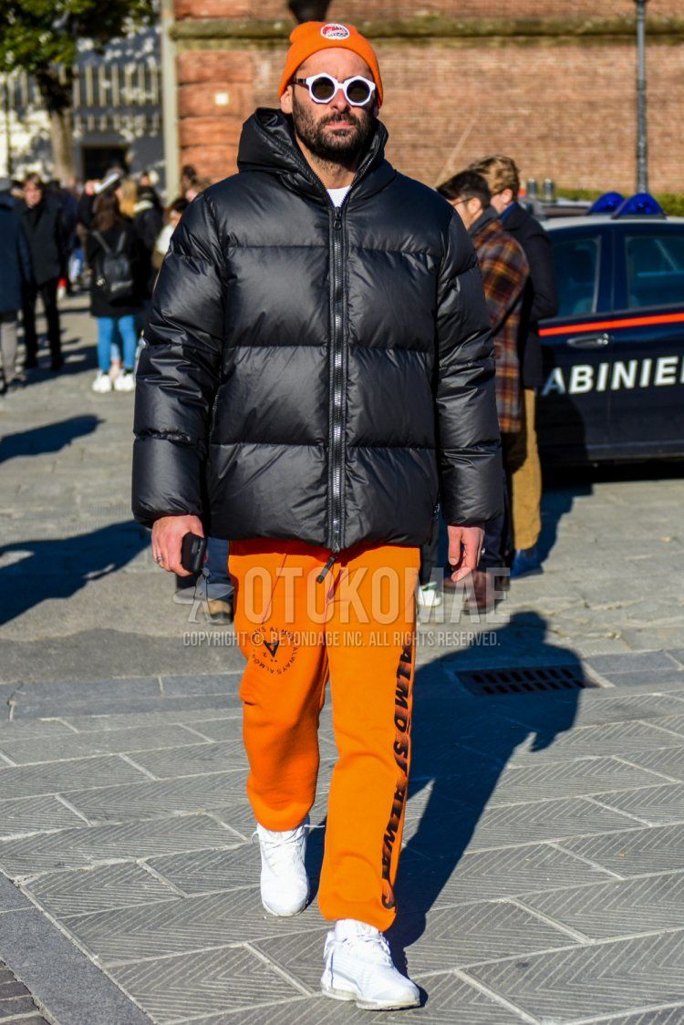 Winter men's coordinate and outfit with orange one-pointed knit cap, plain white sunglasses, plain black down jacket, orange graphic sweatpants, and white low-cut sneakers.