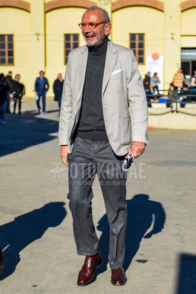 Men's spring and fall outfit with solid beige glasses, solid gray tailored jacket, dark gray solid turtleneck knit, solid gray slacks, solid brown socks, and brown wingtip leather shoes.