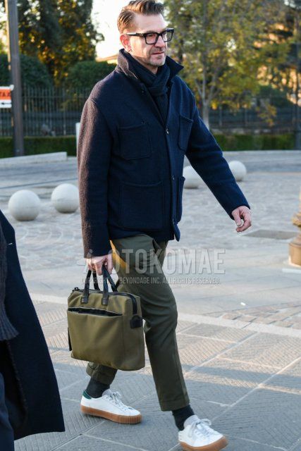 Solid black glasses, solid navy scarf/stall, solid navy shirt jacket, solid olive green chinos, solid olive green ankle pants, solid dark gray socks, white low cut sneakers, solid olive green briefcase/handbag. Men's fall/winter outfits and outfits.