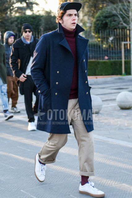 Men's fall/winter coordinate and outfit with solid black jet cap, solid navy Ulster coat, solid red turtleneck knit, solid beige chinos, solid red socks, and white low-cut sneakers.