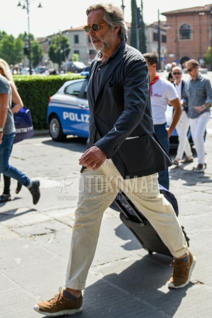 Men's spring, summer, and fall coordinate and outfit with brown tortoiseshell sunglasses, dark gray solid color tailored jacket, gray solid color polo shirt, beige solid color chinos, and brown low-cut sneakers.