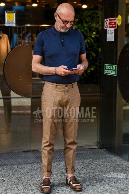 Men's spring and summer coordinate and outfit with brown tortoiseshell glasses, plain navy polo shirt, plain brown chinos and brown monk shoes leather shoes.