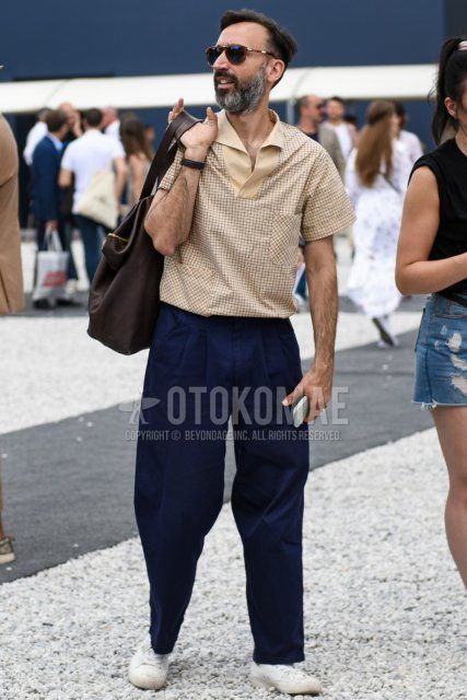 Summer men's summer outfit/coordination with brown tortoiseshell sunglasses, beige checked shirt, plain navy wide pants, plain chinos, plain pleated pants, white low-cut sneakers, and plain brown briefcase/handbag.