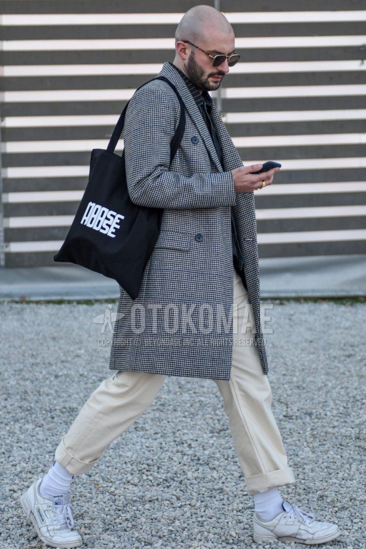 Men's fall/winter coordinate with plain silver sunglasses, gray checked chester coat, dark gray outer shirt jacket, plain beige slacks, plain white socks, white low-cut Reebok sneakers, black graphic briefcase/handbag. Outfit.