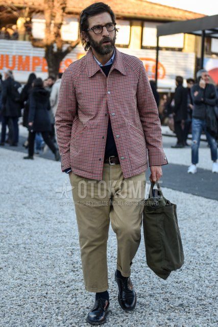 Boston brown tortoiseshell glasses, red checked coach jacket, solid navy sweater, solid light blue shirt, solid brown leather belt, solid beige chinos, solid beige cropped pants, solid black socks, solid black plain toe leather shoes, solid olive green briefcase/handbag with a men's fall/winter outfit.