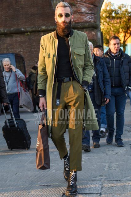 Men's fall/winter outfit with plain silver sunglasses, plain olive green outerwear, plain black turtleneck knit, plain black tape belt, plain beige pleated pants, plain beige chinos, plain beige cropped pants, and Dr. Martens black work boots Outfit.