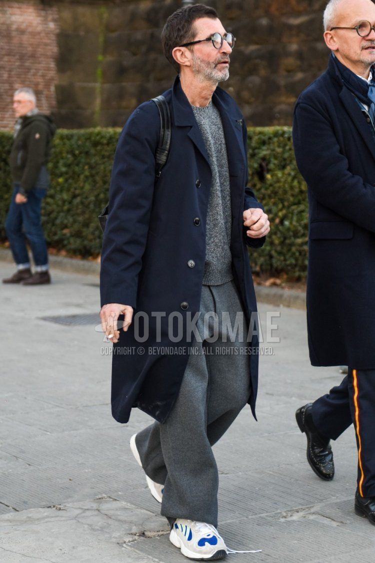 Men's fall/winter coordinate and outfit with round plain black glasses, plain navy stainless steel coat, plain gray sweater, plain gray slacks, and gray low-cut sneakers.