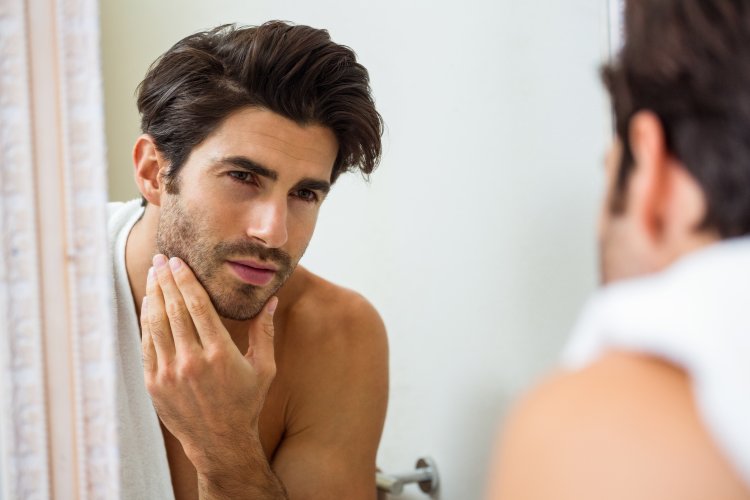 Young man looking in mirror and checking his stubble in bathroom
