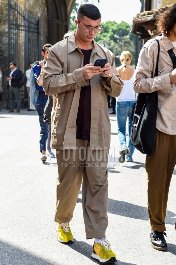 Men's spring, summer, and fall coordinate and outfit with square gold solid sunglasses, solid beige shirt jacket, solid red t-shirt, solid beige cotton pants, solid beige wide-leg pants, solid white socks, and yellow low-cut sneakers.