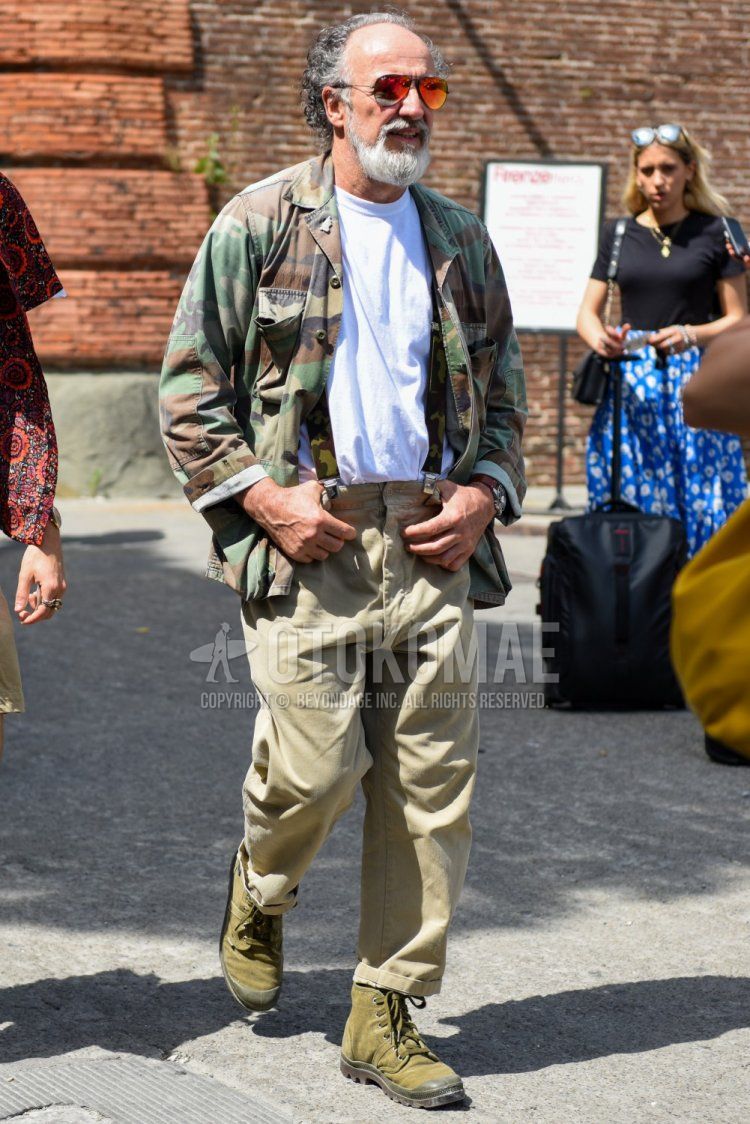 Men's spring, summer, and fall coordinate and outfit with teardrop black and red solid color sunglasses, multi-colored camouflage safari jacket, solid color white t-shirt, multi-colored camouflage suspenders, solid color beige chinos, and olive green boots.