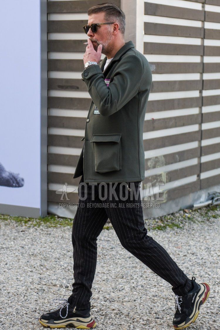 Spring and fall men's coordinate and outfit with olive green solid sunglasses, olive green solid shirt jacket, dark gray striped slacks and Balenciaga Triple S black low-cut sneakers.