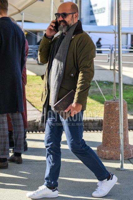 Men's fall/winter outfit with Boston solid gray sunglasses, solid gray scarf/stall, solid olive green outerwear, solid blue denim/jeans, solid black socks, and Adidas Stan Smith white low-cut sneakers.