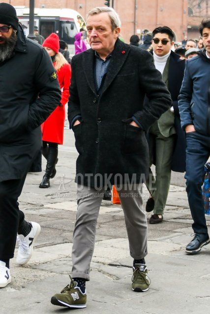 Men's fall/winter coordinate and outfit with plain black chester coat, blue dot shirt, solid green denim/jeans, black dot socks, and New Balance olive green low-cut sneakers.