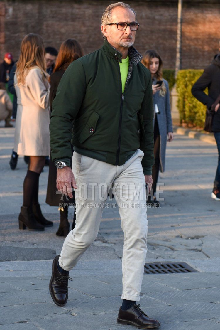 Men's fall/winter outfit with solid black glasses, solid olive green swing top, solid yellow sweater, solid beige chinos, solid navy socks, and black plain toe leather shoes.