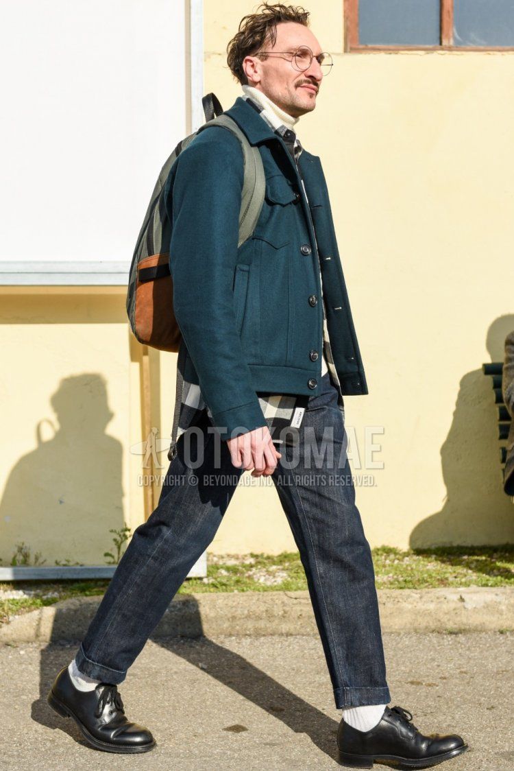 Men's fall/winter outfit with plain silver glasses, plain gray trucker jacket, white/black checked shirt, plain white turtleneck knit, plain navy denisla, plain white socks, black plain toe leather shoes, and plain olive green backpack.