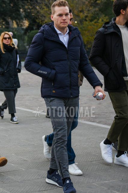 Men's coordinate and outfit with solid navy down jacket, solid navy hooded coat, solid light blue shirt, gray checked slacks, solid black socks, and New Balance navy low-cut sneakers.