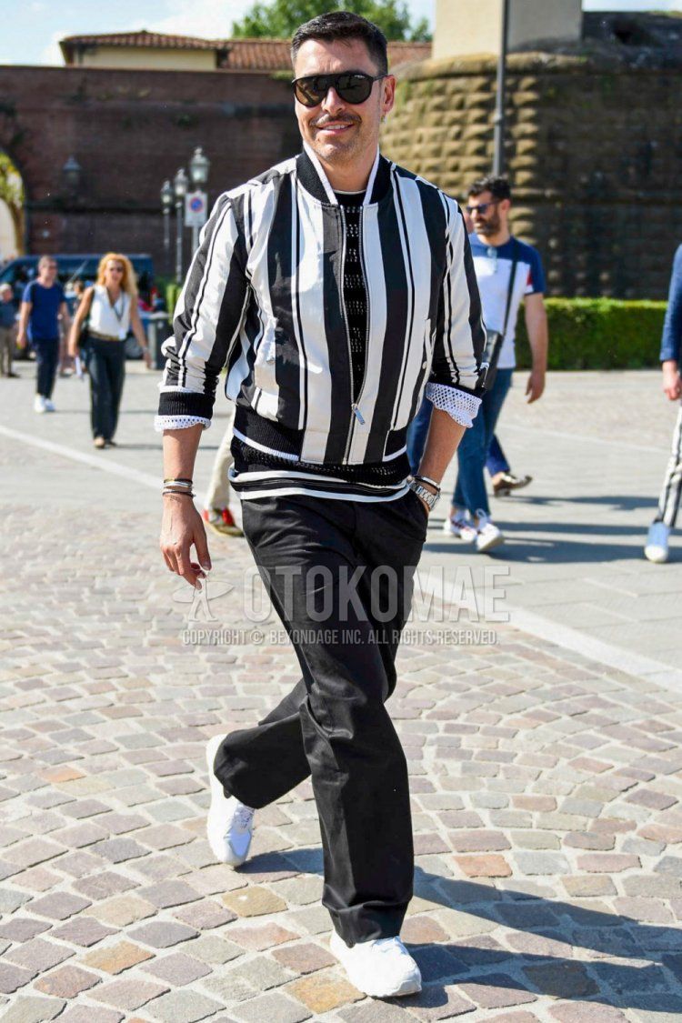 Men's spring and fall coordinate and outfit with plain black sunglasses, white and black striped MA-1, black striped T-shirt, plain black wide pants, and white low-cut sneakers.