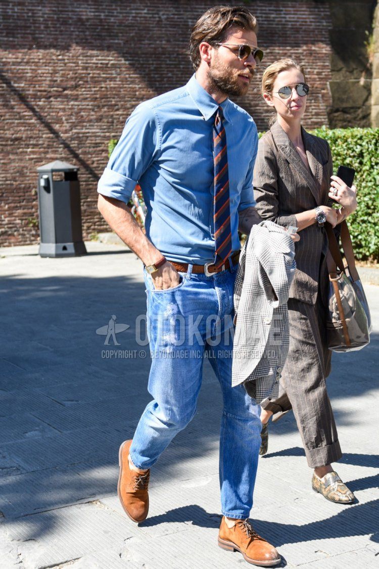 Men's spring/summer/fall outfit with gold/black solid sunglasses, blue solid denim/chambray shirt, brown solid leather belt, blue solid denim/jeans, brown suede shoes leather shoes, brown/navy regimental tie.