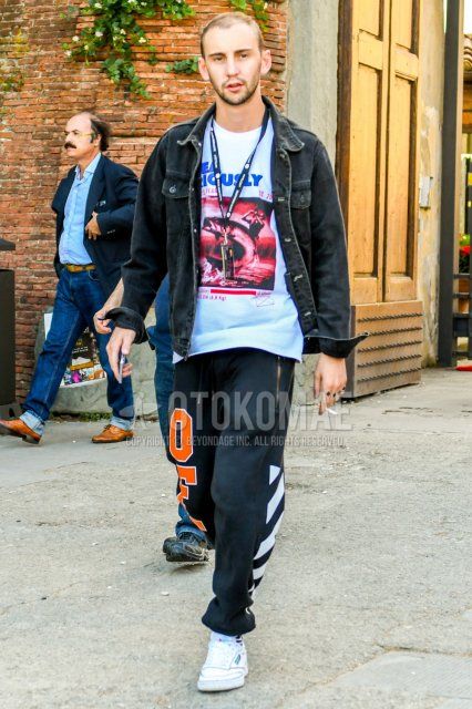 Men's spring and fall coordinate and outfit with plain gray denim jacket, white graphic t-shirt, off-white black graphic sweatpants, and white low-cut Reebok sneakers.