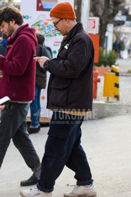 Men's fall/winter outfit with plain orange knit cap, brown tortoiseshell glasses, plain dark gray outerwear, plain beige sweater, plain navy cargo pants, and white low-cut Reebok sneakers.