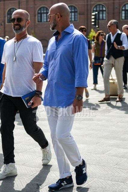 Men's spring and fall coordinate and outfit with gold plain sunglasses, light blue dotted shirt, plain white cotton pants, and New Balance navy low-cut sneakers.
