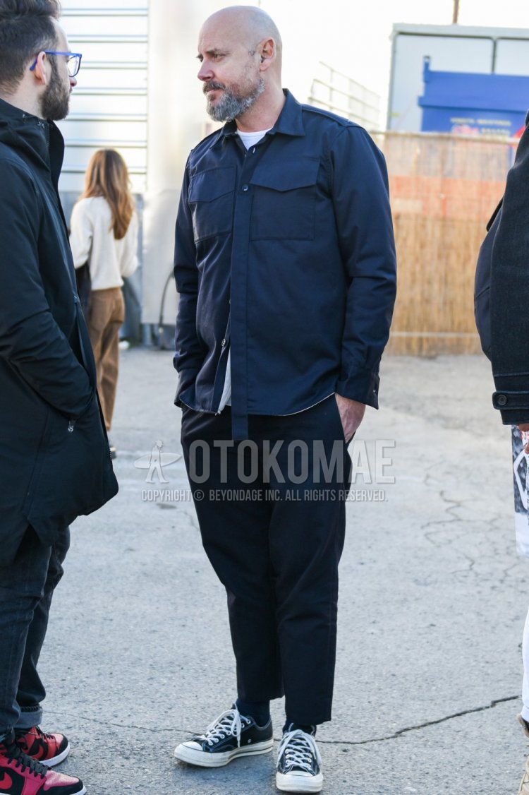 Spring and fall men's coordinate and outfit with dark gray solid shirt jacket, solid white t-shirt, dark gray solid slacks, dark gray solid cropped pants, solid black socks, and black low-cut sneakers.