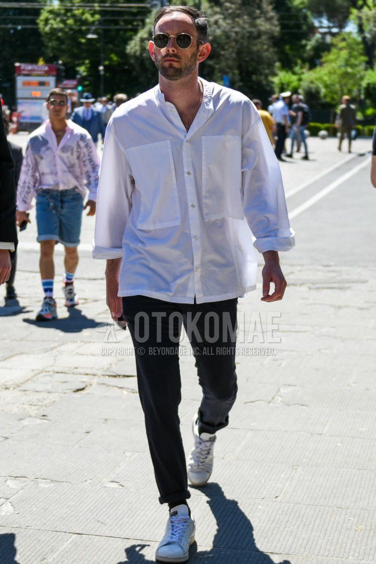 Men's spring/summer coordinate and outfit with round gold and black solid sunglasses, solid white shirt, solid black cotton pants, solid black socks, and white low-cut Adidas Stan Smith sneakers.