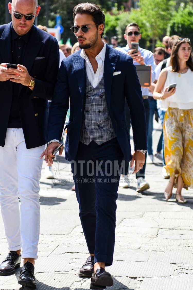 Men's spring, summer, and fall coordinate and outfit with plain silver sunglasses, plain white shirt, gray checked gilet, brown coin loafer leather shoes, and plain navy suit.