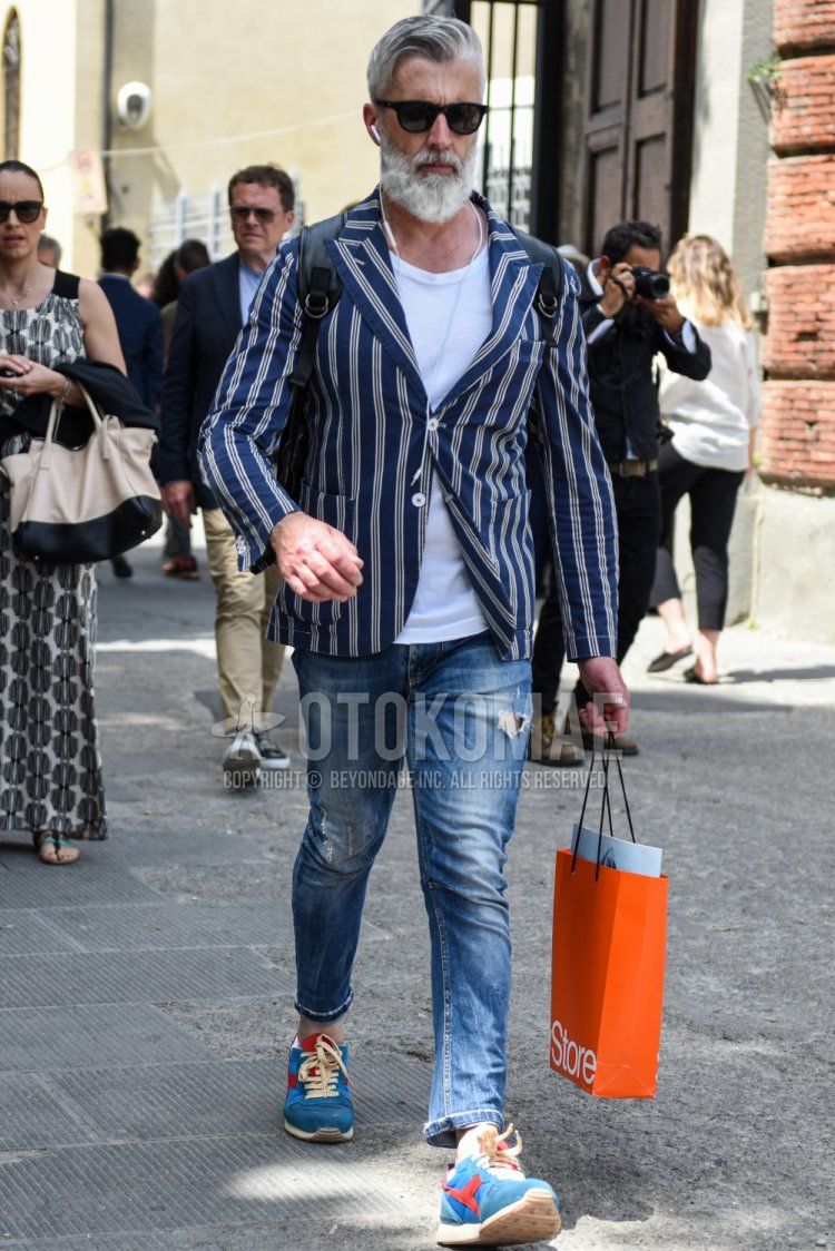 Men's spring, summer, and fall coordinate and outfit with plain black sunglasses, navy striped tailored jacket, plain white t-shirt, plain blue damaged jeans, and Diadora blue low-cut sneakers.