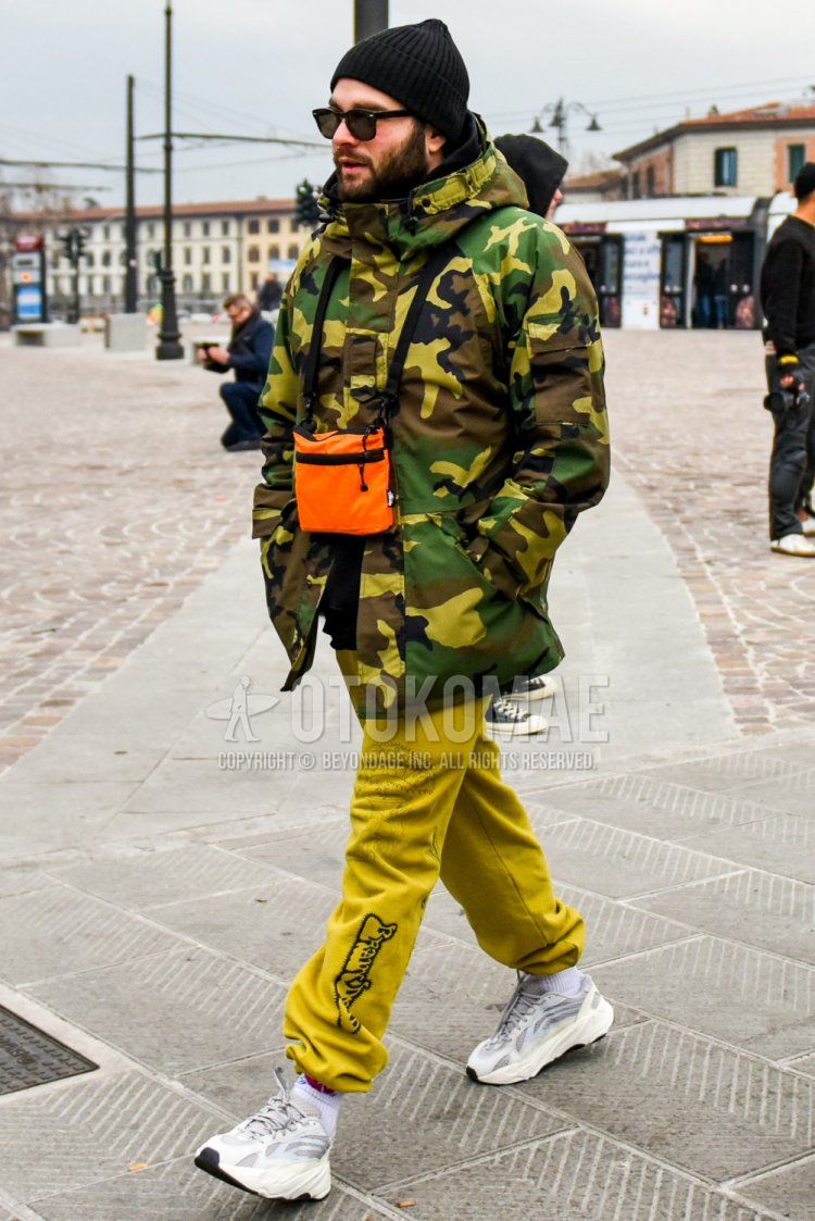 Solid black knit cap, solid black Wellington sunglasses, olive green camouflage down jacket, solid black hoodie, yellow graphic sweatpants, solid white socks, Adidas Easy Boost 700 white low cut sneakers, solid orange body bag with the following men's fall/winter outfits and outfits.