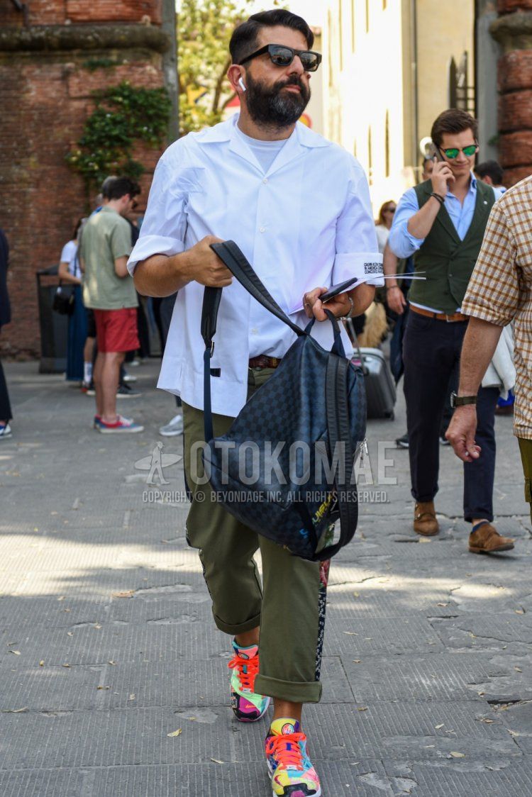 Men's spring/summer/fall outfit with plain black Wellington sunglasses, plain white shirt, plain white t-shirt, plain brown leather belt, plain olive green cotton pants, Nike multi-colored low-cut sneakers, Louis Vuitton black checked backpack.