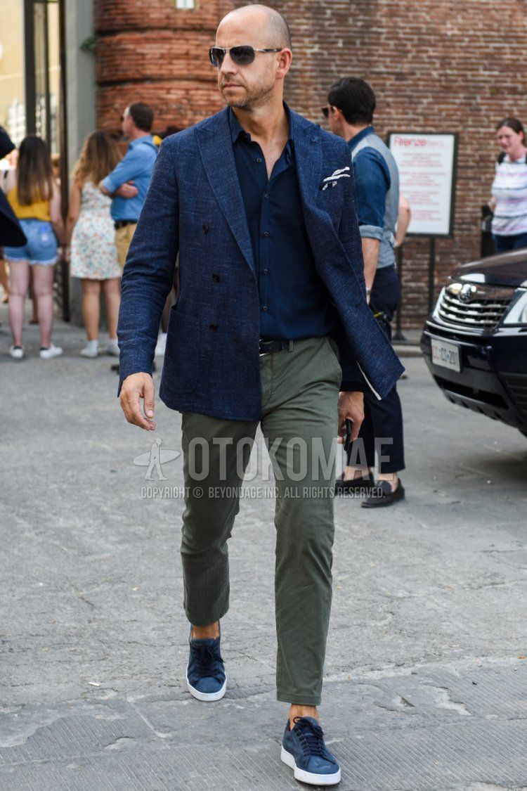 Men's spring/summer/autumn coordinate and outfit with plain black/silver sunglasses, plain navy tailored jacket, plain navy shirt, plain black leather belt, plain olive green ankle pants, plain chinos, and gray low-cut sneakers.