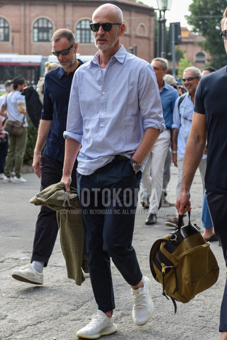 Men's spring and summer coordinate and outfit with plain black sunglasses, light blue striped shirt, plain white t-shirt, plain navy slacks and Adidas Yeezy Boost 350 V2 white low-cut sneakers.