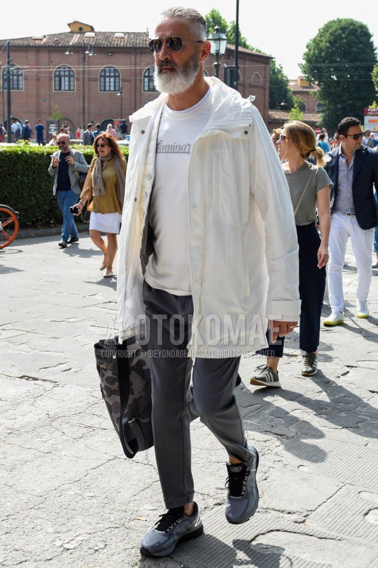 Men's spring/fall outfit with plain silver sunglasses, plain white hooded coat, white graphic t-shirt, plain gray slacks, gray low-cut sneakers, and gray camouflage briefcase/handbag.
