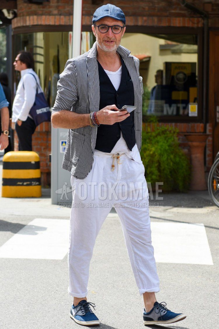 Men's spring, summer, and fall outfits with plain navy cap, plain black glasses, black/gray striped tailored jacket, plain black gilet, plain white shirt, plain white t-shirt, plain white easy pants, and blue low-cut sneakers.