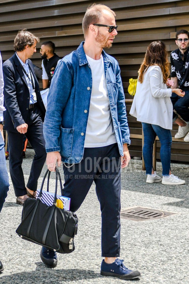Men's spring/summer/fall outfit with plain Ray-Ban Wayfarer sunglasses, plain blue denim jacket, plain white t-shirt, plain navy slacks, navy low-cut sneakers, and plain black briefcase/handbag.