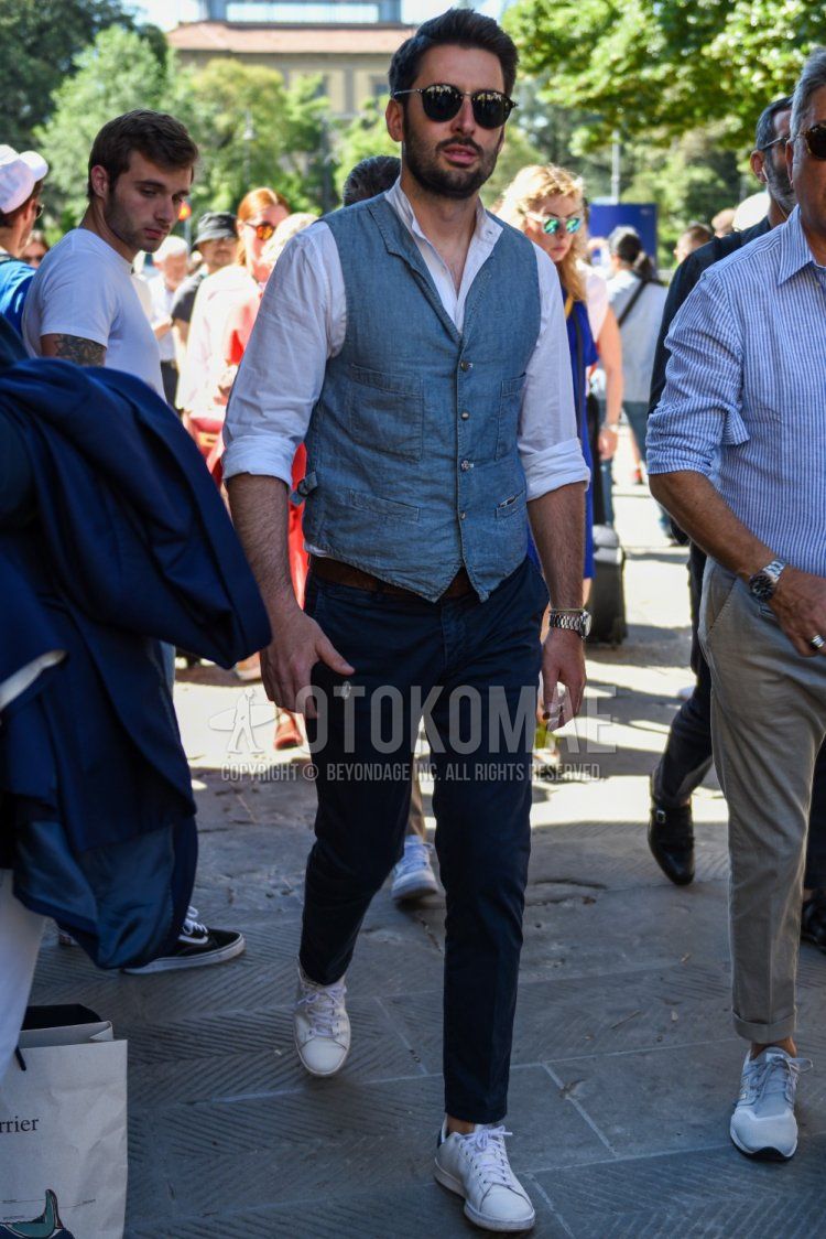 Men's spring/summer outfit with plain black sunglasses, plain gray gilet, plain white shirt with band collar, plain brown leather belt, plain navy chinos, and Adidas Stan Smith white low-cut sneakers.