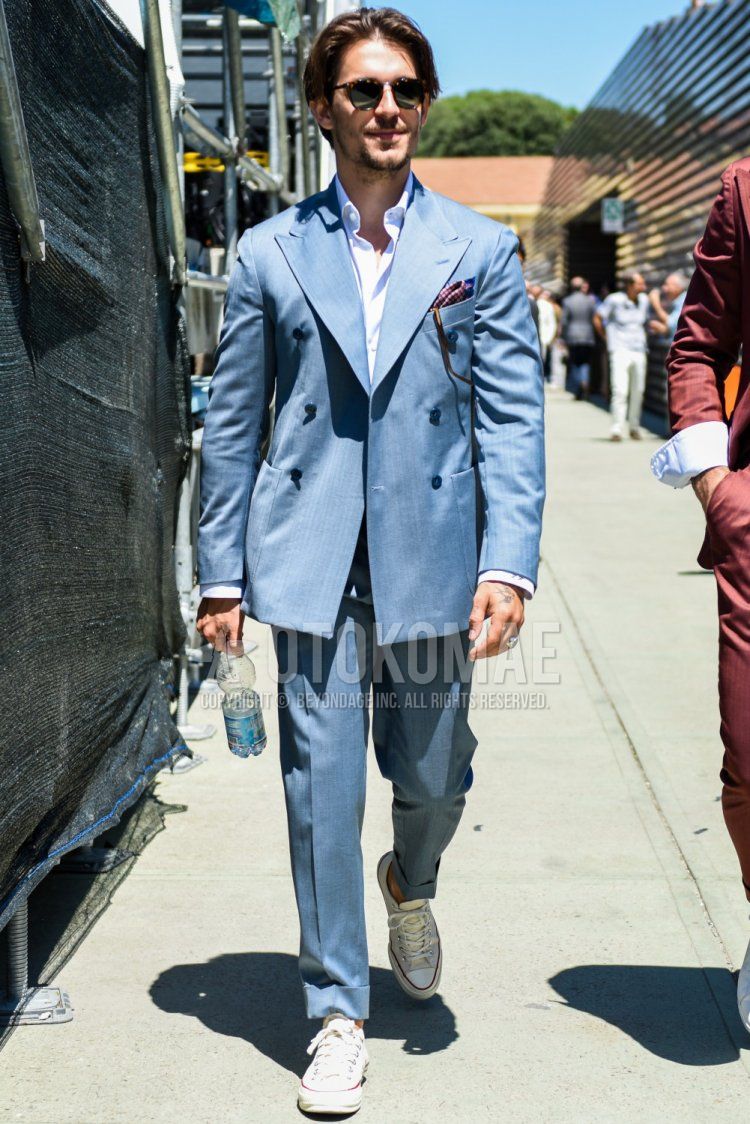Men's spring, summer, and fall coordination and outfit with brown tortoiseshell sunglasses, plain white shirt, white low-cut Converse All Star sneakers, and plain light blue suit.