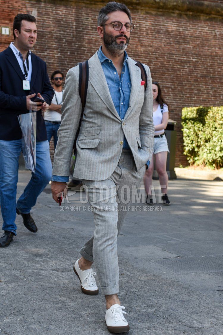 Men's spring/summer/autumn coordination and outfit with plain black glasses, plain blue denim/chambray shirt, white low-cut sneakers, and gray striped suit.