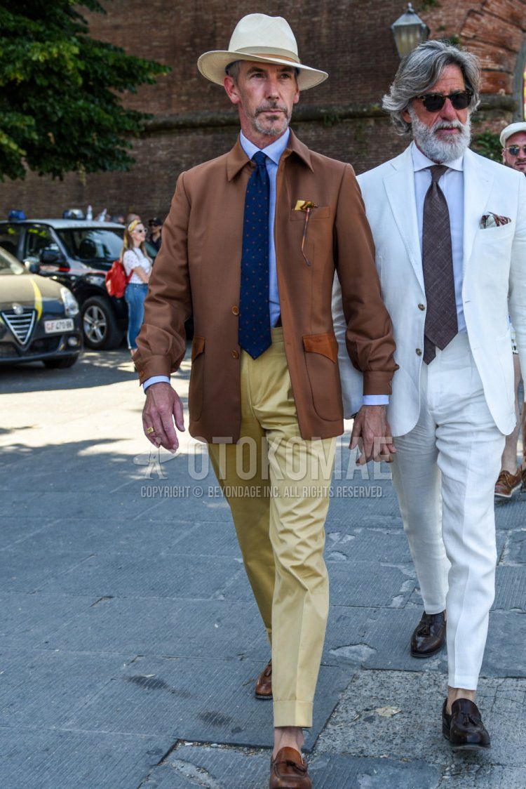 Men's spring and fall outfit and outfit with solid beige hat, solid brown shirt jacket, solid light blue shirt, solid beige beltless pants, brown tassel loafer leather shoes, and blue dot tie.