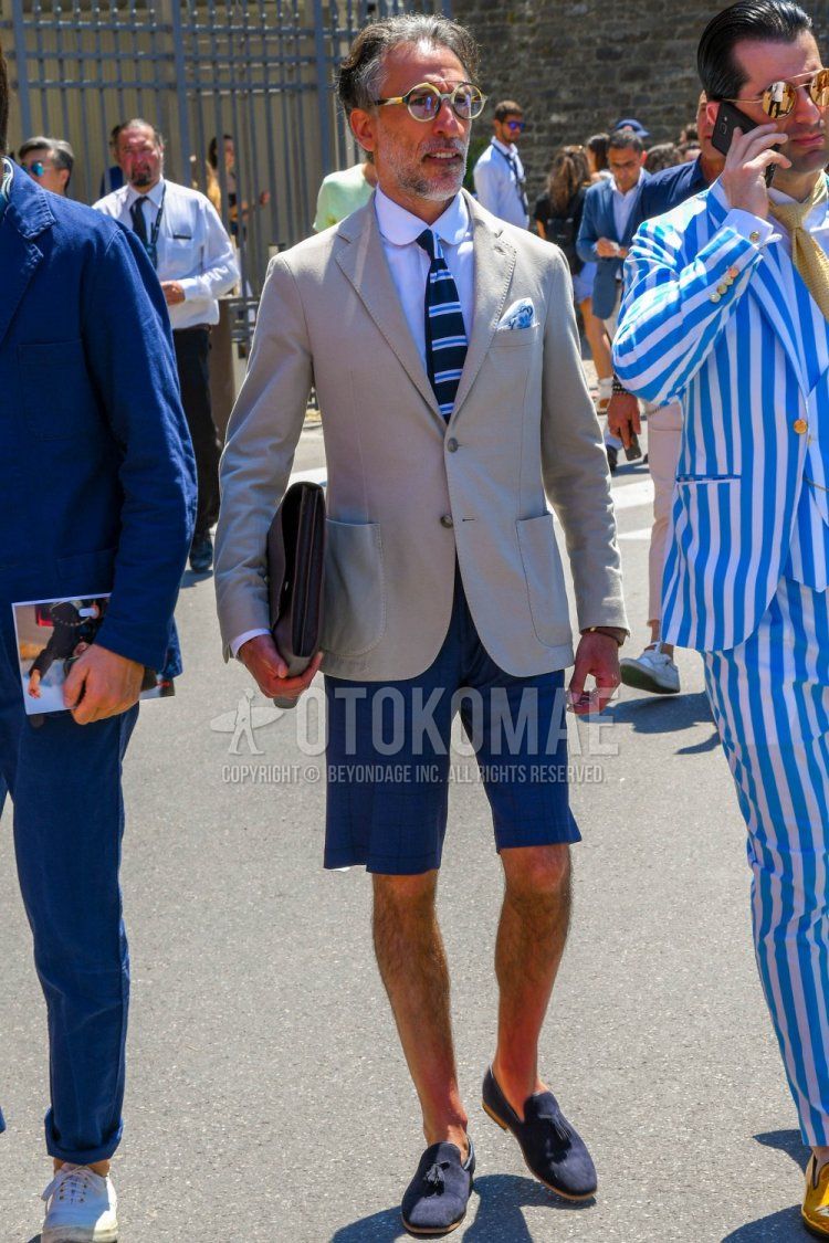 Men's spring/summer/fall outfit with plain glasses, plain white tailored jacket, plain white shirt, blue checked shorts, checked slacks, navy tassel loafers leather shoes, suede shoes leather shoes, plain brown clutch/second bag/drawstring bag. Outfit.